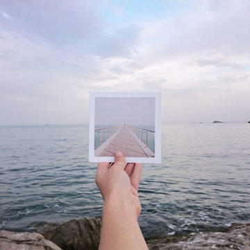 Human hand holding instant print transfer photo in front of the sea 