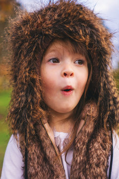 Close-up Portrait of young girl standing outdoors wearing a fluffy trapper hat pulling funny faces