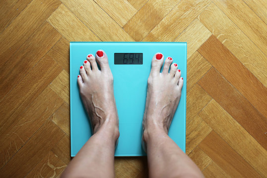 Overhead view of a woman standing barefoot on bathroom scales weighing herself