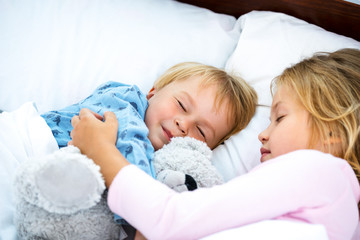 Obraz na płótnie Canvas Little girl and boy sleeping on white bed