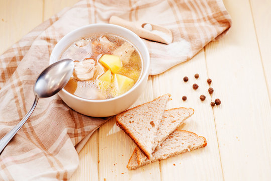 healthy hot lunch , chicken soup with potatoes , carrots , chicken breast , spices and rye bread on a wooden background