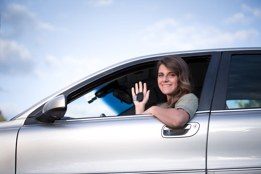 Smiling Teenage girl sitting in a car leaning out of an open window holding the keys to her new car