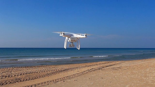 White drone with hovering over a sandy beach