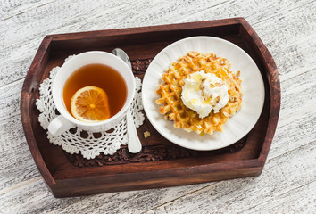 Lemon tea and waffles with ice cream, honey and nuts in vintage tray on a light wooden board