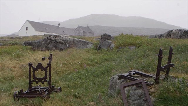 Abandoned building with rusted cast iron equipment in the foreground during a snowfall in Hebron, Newfoundland and Labrador. Slow Motion