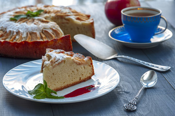 Piece of apple pie on plate with jam, tea cup