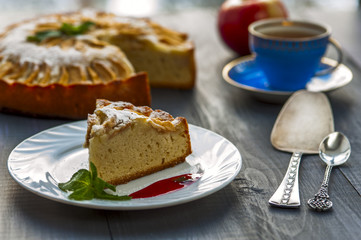 Piece of apple pie on plate with jam, tea cup