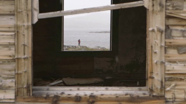Expeditioner seen through the window of an abandoned house in Hebron, Newfoundland and Labrador on a snowy day. Slow Motion