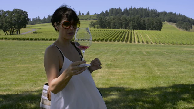 Woman sipping a glass of Rose wine, with a vineyard behind her