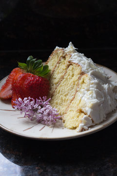 Frosted vanilla cake with strawberry and lilac on brown plate closeup dark background