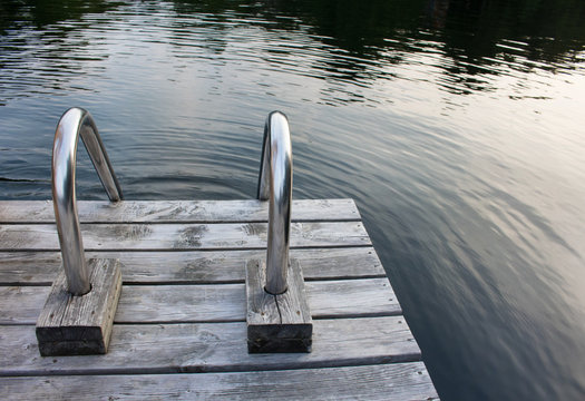 Closeup of a steel ladder on a wooden dock leading into a northern lake