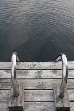 Closeup of a steel ladder on a wooden dock leading into a northern lake still life