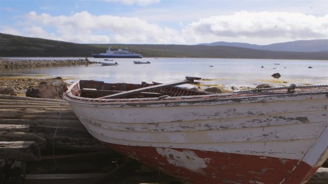 Fishing boat sitting on the shore of Conche, Newfoundland & Labrador with an anchored cruise ship in the background.