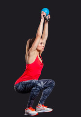 Young woman smiling while using kettlebells against a gray background