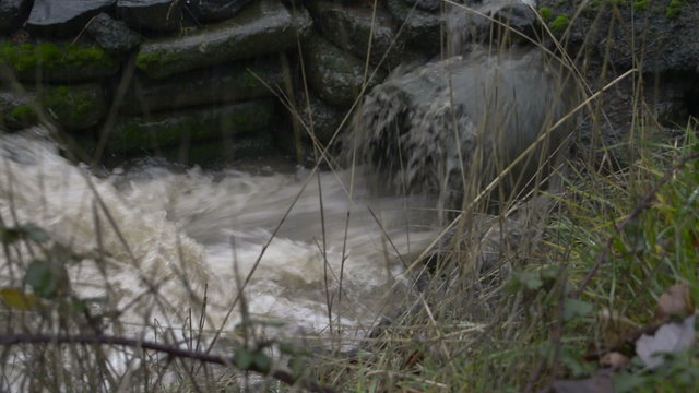 Close up of water surging out of a pipe into a roadside drainage ditch