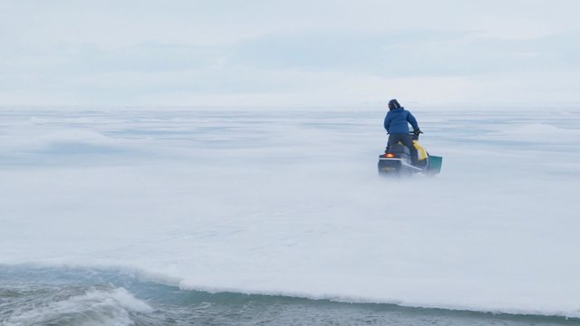 Man on ski-doo crossing frozen sea. Pan