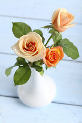 Bouquet of orange roses in vase on blue wooden background