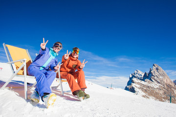two snowboarders on top of the mountain having fun sitting on chair chaise lounge