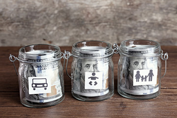 Rolls of dollar banknotes for different needs in glass jars on wooden table