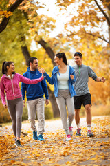 A lively group of young friends enjoys a refreshing jog in the park during the vibrant autumn...