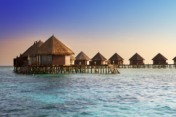 Island in ocean, overwater villas at the time sunset.