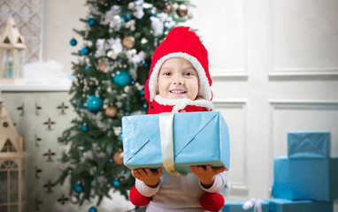 Obraz na płótnie Canvas Cute little boy holding a gift against Christmas tree in background 