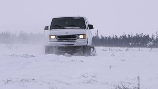 Van with caterpillar tracks traveling through arctic tundra.