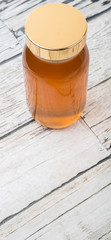 Pure honey in a tall glass jar over wooden background