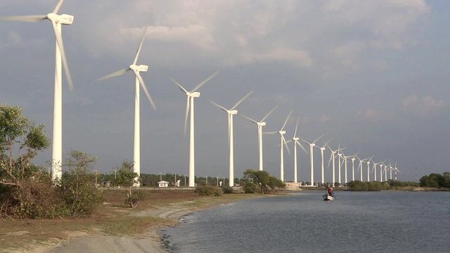 Sri Lankan fishermen punting their boat along Puttalam Lagoon with wind farm turbines rotating near the waters edge
