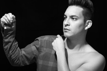 Hispanic male putting on square pattern shirt, one arm dressed the other naked, black and white edition