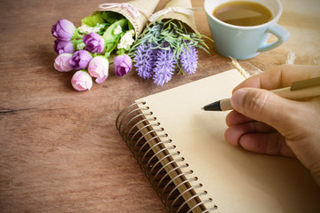 Cup of coffee with flower and blank notebook on wooden table