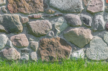 Wall made of irregular granite stones with green grass