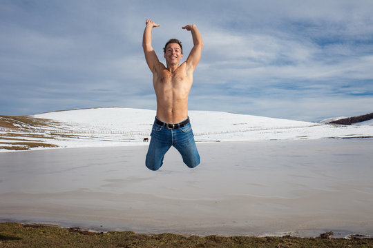 Uomo a torso nudo salta sulle rive di un lago ghiacciato