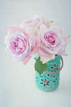 Beautiful pink roses in a blue ceramic vase on a light background. 