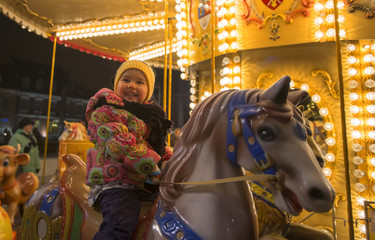 Fototapeta na wymiar Adorable little girl on a carousel at Christmas market