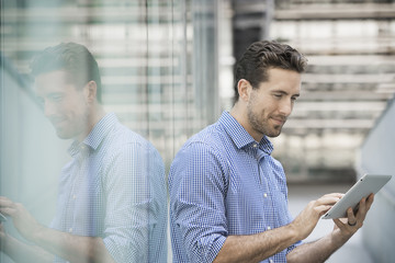 A man standing outside a building with large glass exterior panels, using a digital tablet. 