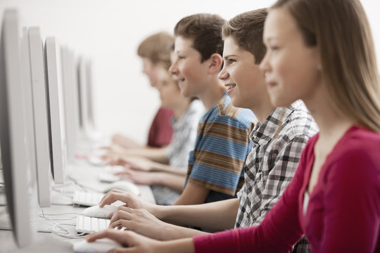 A group of young people, boys and girls, students in a computer class working at screens. 