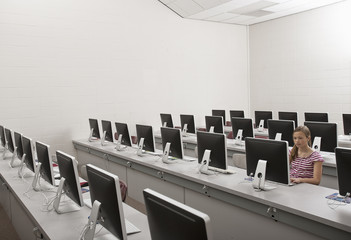 A school room, a computer lab with rows of screens and seating. A young person seated working at a terminal.