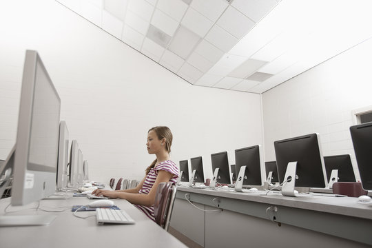 A school room, a computer lab with rows of screens and seating. A young person seated working at a terminal.