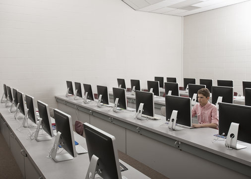 A school room, a computer lab with rows of screens and seating. A young person seated working at a terminal.