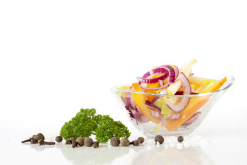 Salad with fresh onion and vegetables in glass plate, green parsley, peper, rosemary on white...