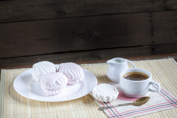 Cup of hot coffee with marshmallow, milk and flowers on wooden table. Vintage still life.