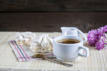Cup of hot coffee with marshmallow, milk and flowers on wooden table. Vintage still life.