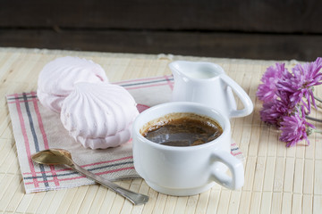 Cup of hot coffee with marshmallow, milk and flowers on wooden table. Vintage still life.