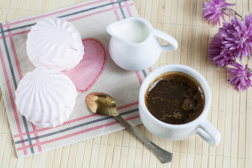 Cup of hot coffee with marshmallow, milk and flowers on wooden table. Vintage still life.