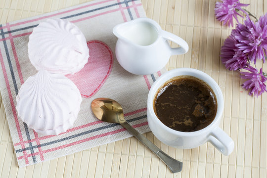 Cup of hot coffee with marshmallow, milk and flowers on wooden table. Vintage still life.