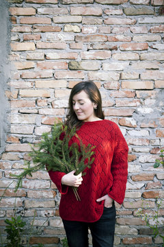 A woman holding in her arms pine branches for to make a christmas garland in front of a brick wall