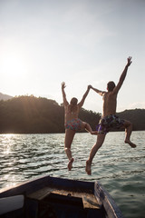 Young couple jumping on the edge of a boat