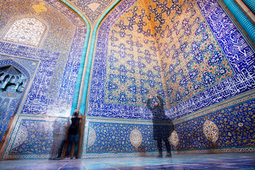 People in blue and yellow colors mosque with tiles on walls in Iran