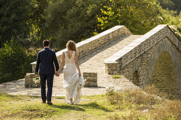 Fototapeta premium Rear view of Bride and groom walking toward a bridge.